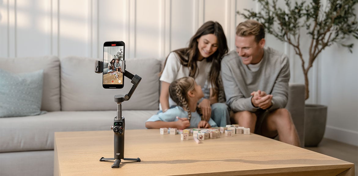 Rodzice z córką na kanapie nagrywają film stojącym na stole gimbalem DJI Osmo Mobile 8